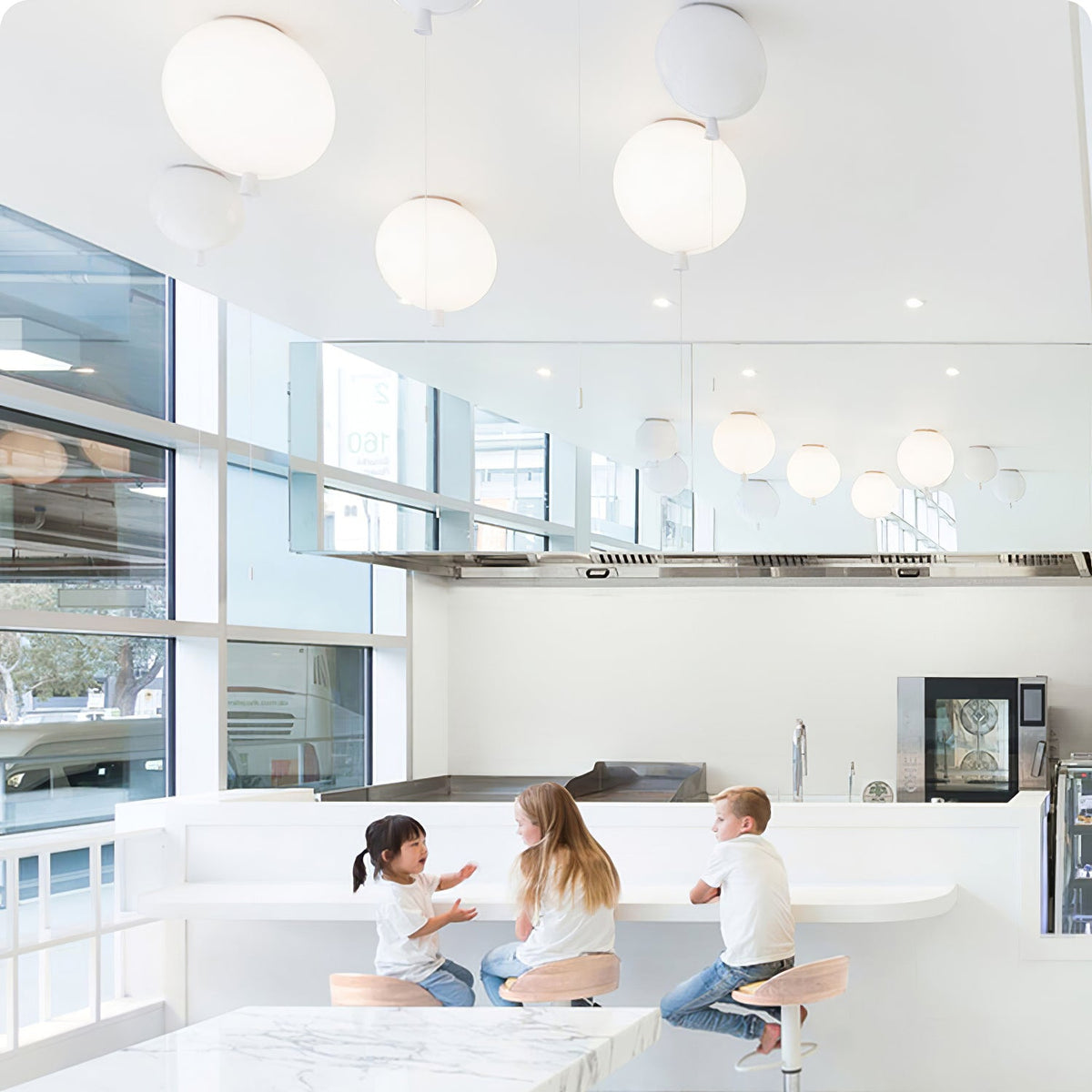 Several plain round globe pendants hang above a kitchen counter where children sit, a different design from this Clérachic balloon light.
