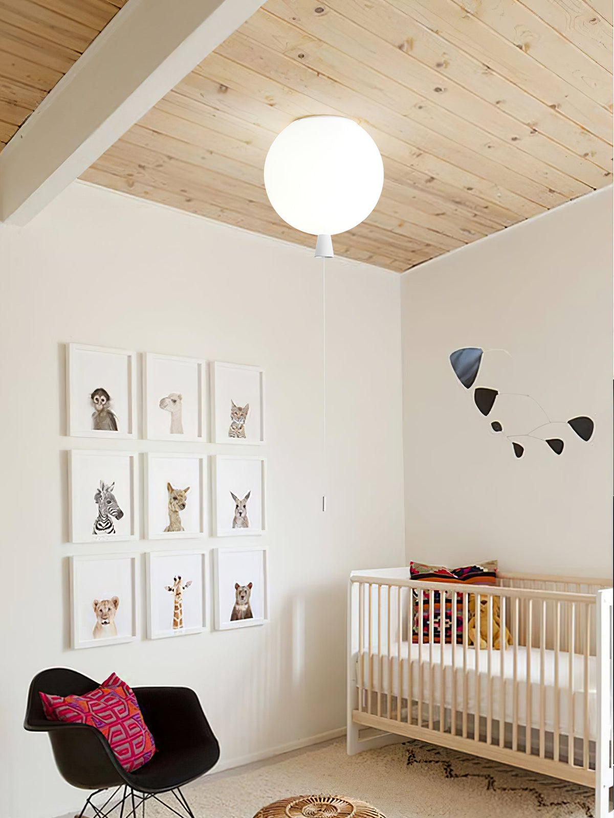 A single round white globe light is mounted on a wood-panelled sloped ceiling in a nursery with framed animal prints, near this Clérachic balloon range.