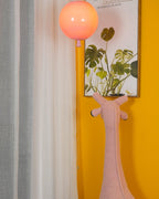 A single peach-toned Clérachic balloon light hangs near a yellow wall, a botanical print and a knitted animal wall hook.