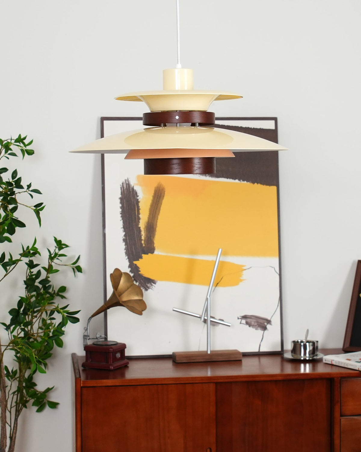 A beige Clérachic pendant hangs in front of a dark console styled with framed art.