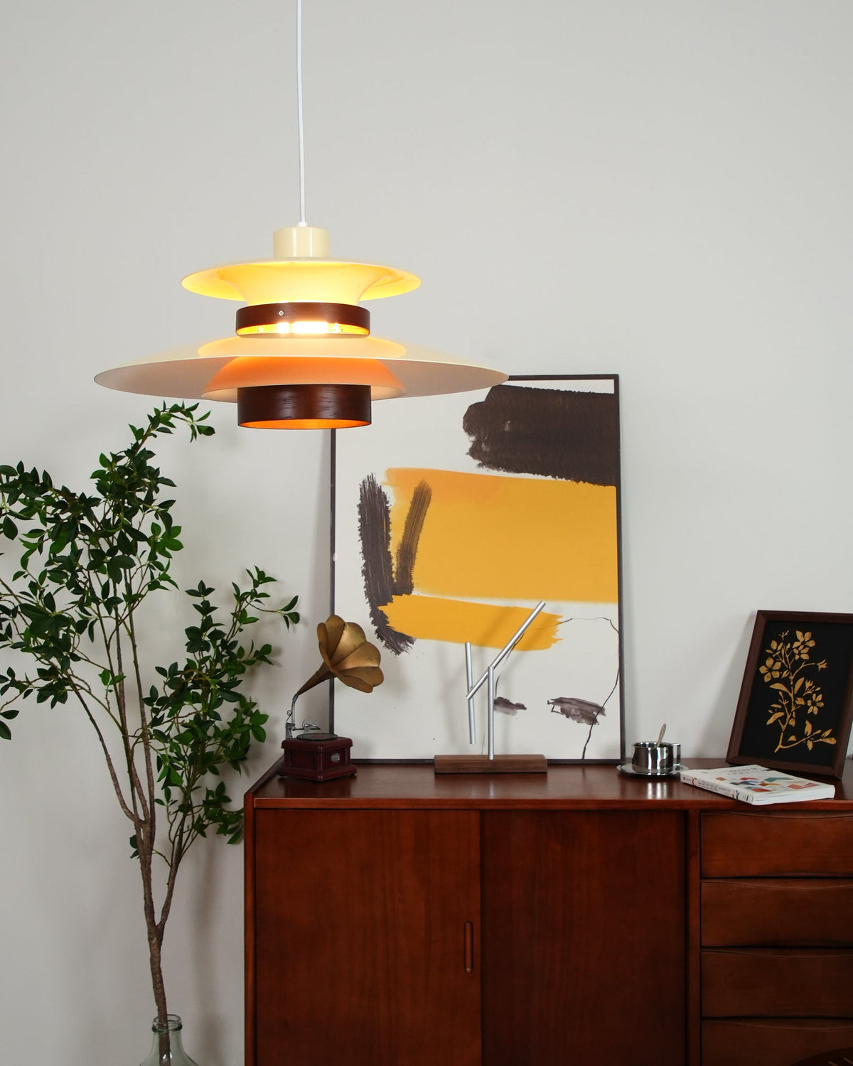 A lit beige Clérachic pendant hangs low beside a sideboard styled with a gramophone and art.