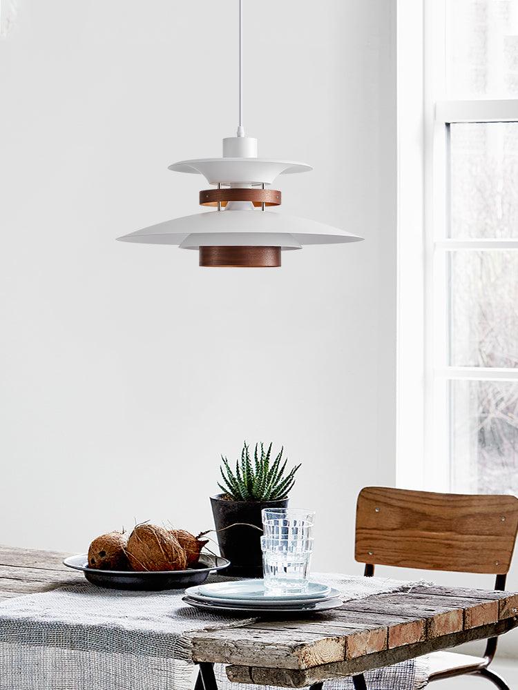 A white Clérachic pendant lights a rustic wood table set with croissants and glassware.