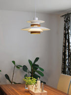 A white Clérachic pendant hangs over a wooden table with potted greenery nearby.