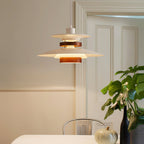 A white Clérachic pendant with a walnut ring hangs lit near a doorway and potted plant.