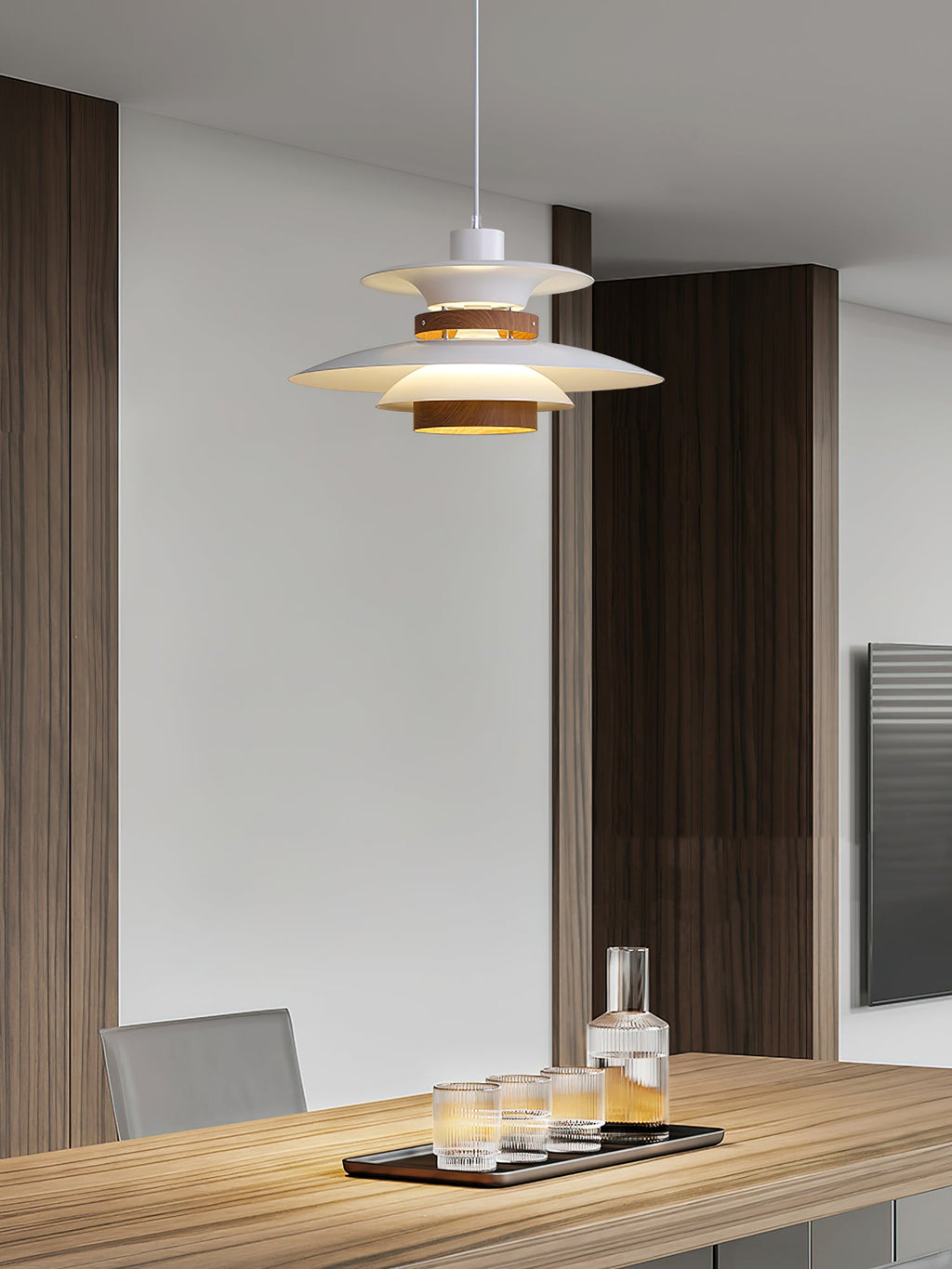 A white Clérachic pendant lights a wooden dining table against dark panelled walls.