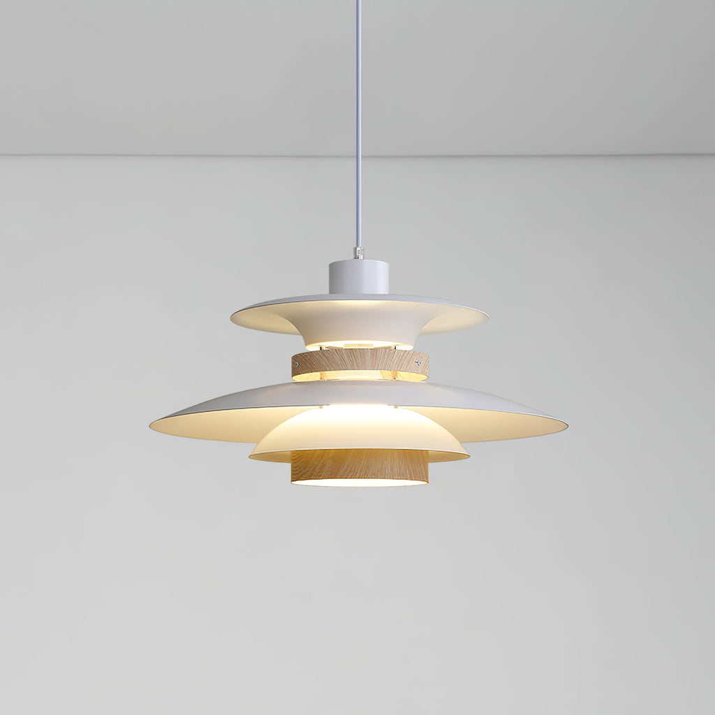 A lit beige Clérachic pendant with tiered metal shades and a walnut ring, on a plain backdrop.