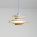 A lit beige Clérachic pendant with tiered metal shades and a walnut ring, on a plain backdrop.