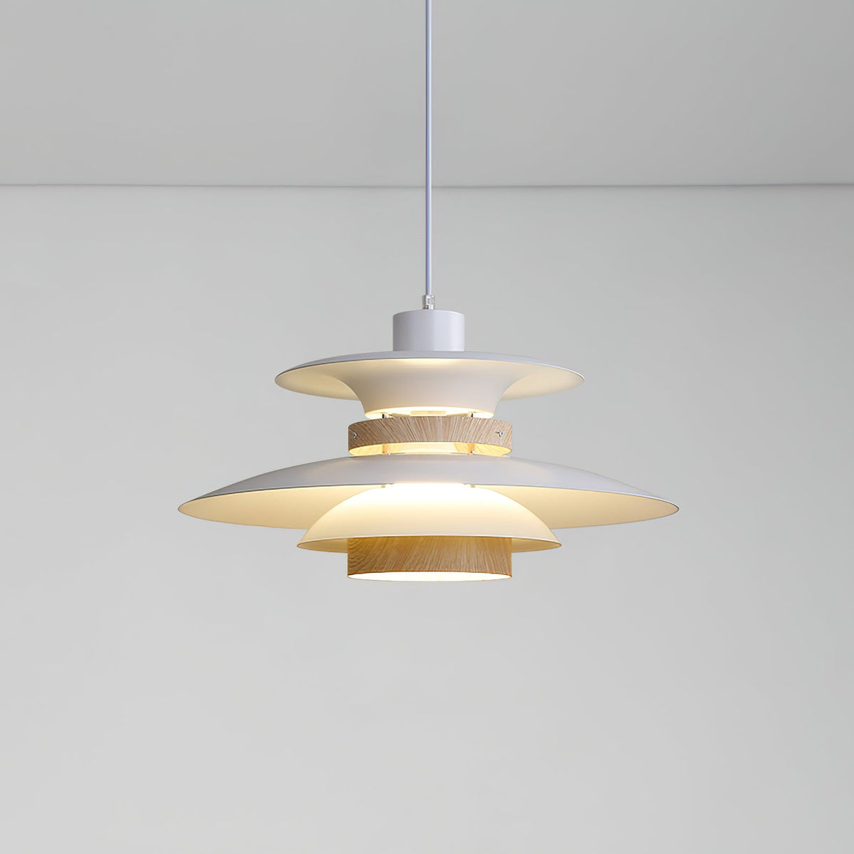 A lit beige Clérachic pendant with tiered metal shades and a walnut ring, on a plain backdrop.