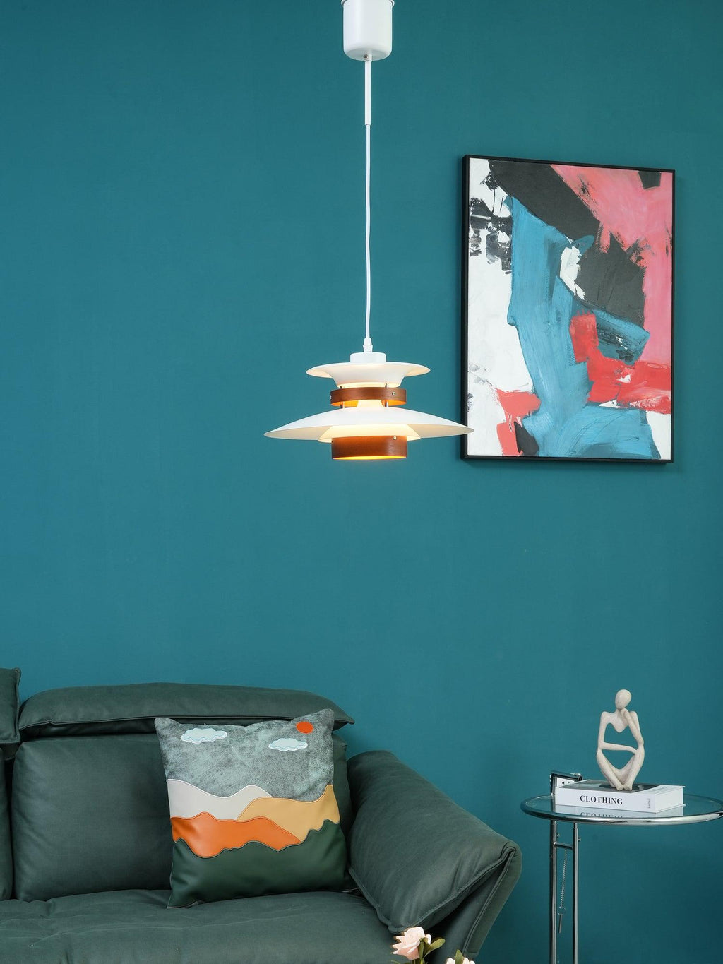 A white Clérachic pendant hangs in a teal living room above a green sofa and cushion.