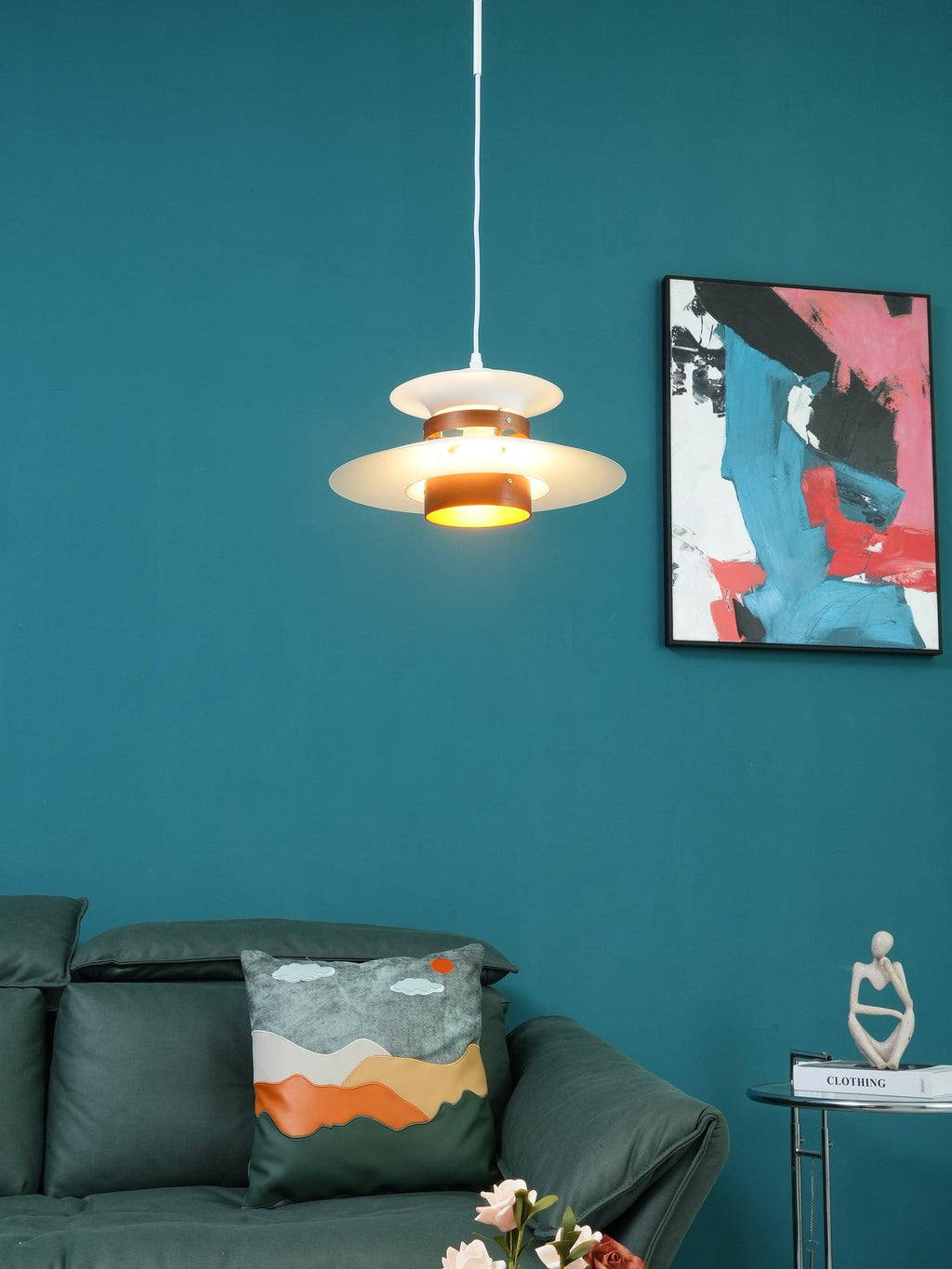 A beige Clérachic pendant hangs against a teal wall beside a bold framed print.