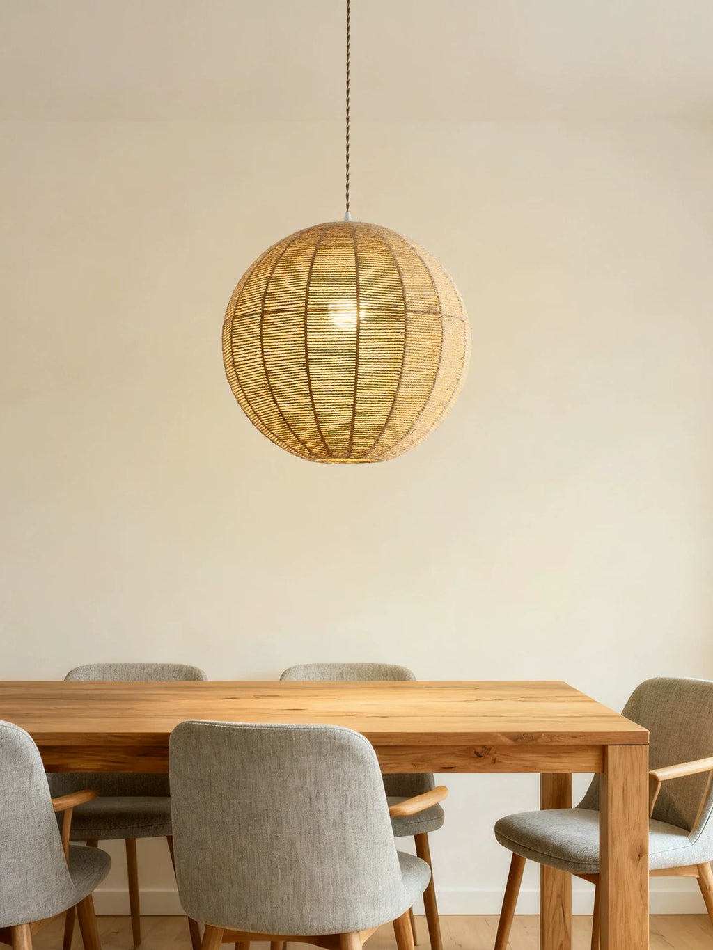 A hemp rope Clérachic pendant hangs above a wood dining table with grey upholstered chairs against a plain wall.