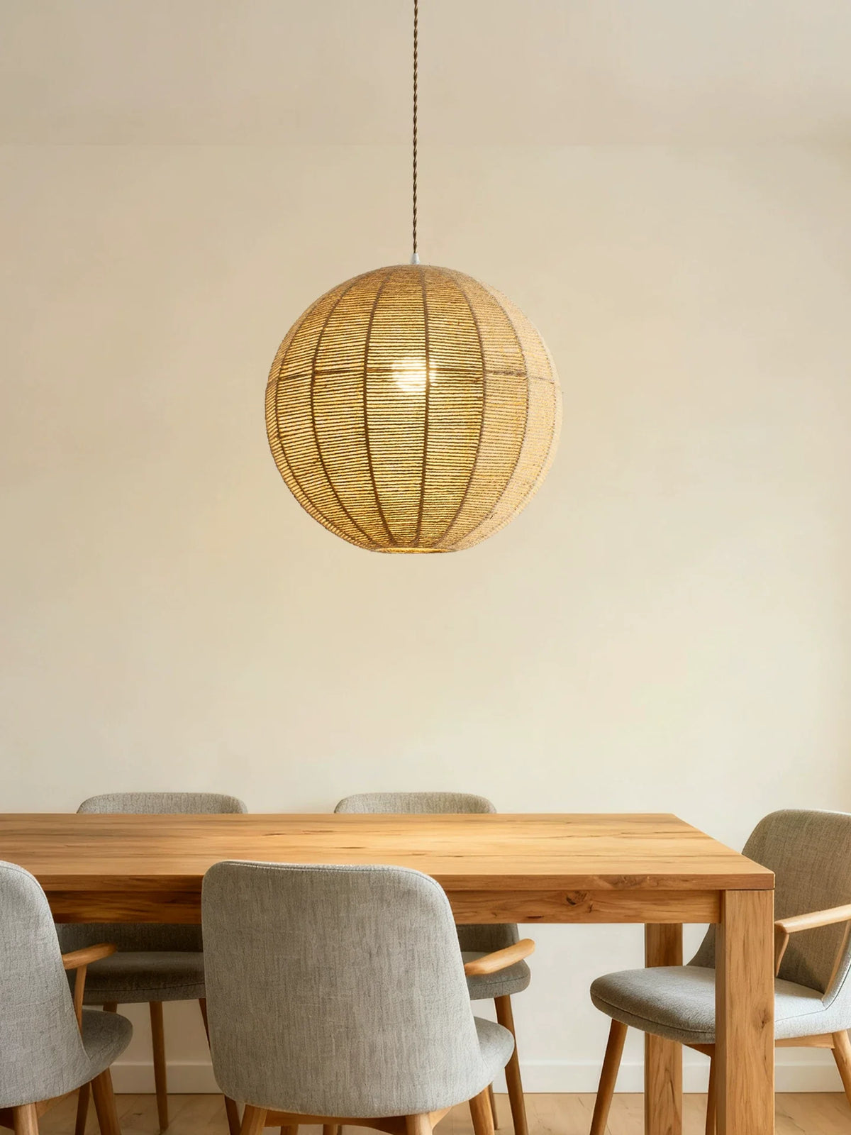 A hemp rope Clérachic pendant hangs above a wood dining table with grey upholstered chairs against a plain wall.