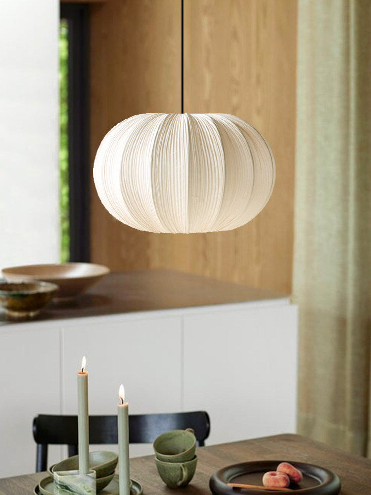 This Clérachic pendant's round pleated shade hangs above a wood dining table set with candles and small ceramic bowls.