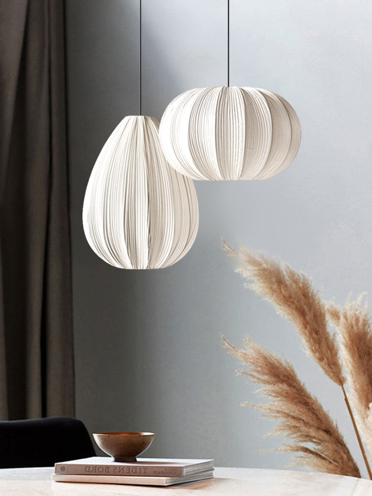 Two Clérachic pendants, one egg-shaped and one round, hang beside a dark curtain and a bundle of pampas grass.