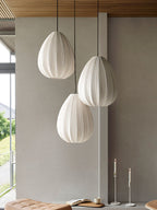 Three egg-shaped Clérachic pendants hang at staggered heights in a room with a concrete wall and tall candlesticks.