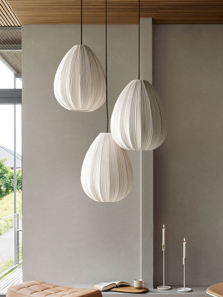 Three egg-shaped Clérachic pendants hang at staggered heights in a room with a concrete wall and tall candlesticks.