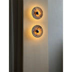 Macro crop of two Clérachic marble wall lights glowing strongly amber, their dark centre knobs and veining lit from behind.