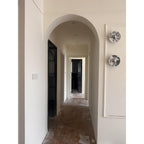 A distant hallway view shows two unlit Clérachic marble wall lights mounted on a wall beyond an arched doorway.