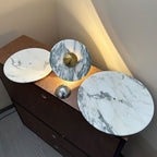 Three marble disc finishes for the Clérachic wall light lie flat on a dresser beside a loose chrome centre knob, each veined differently.