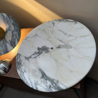 Overhead close-up of a warm-toned Clérachic marble disc lying flat, its small centre hole visible before the knob is fitted.