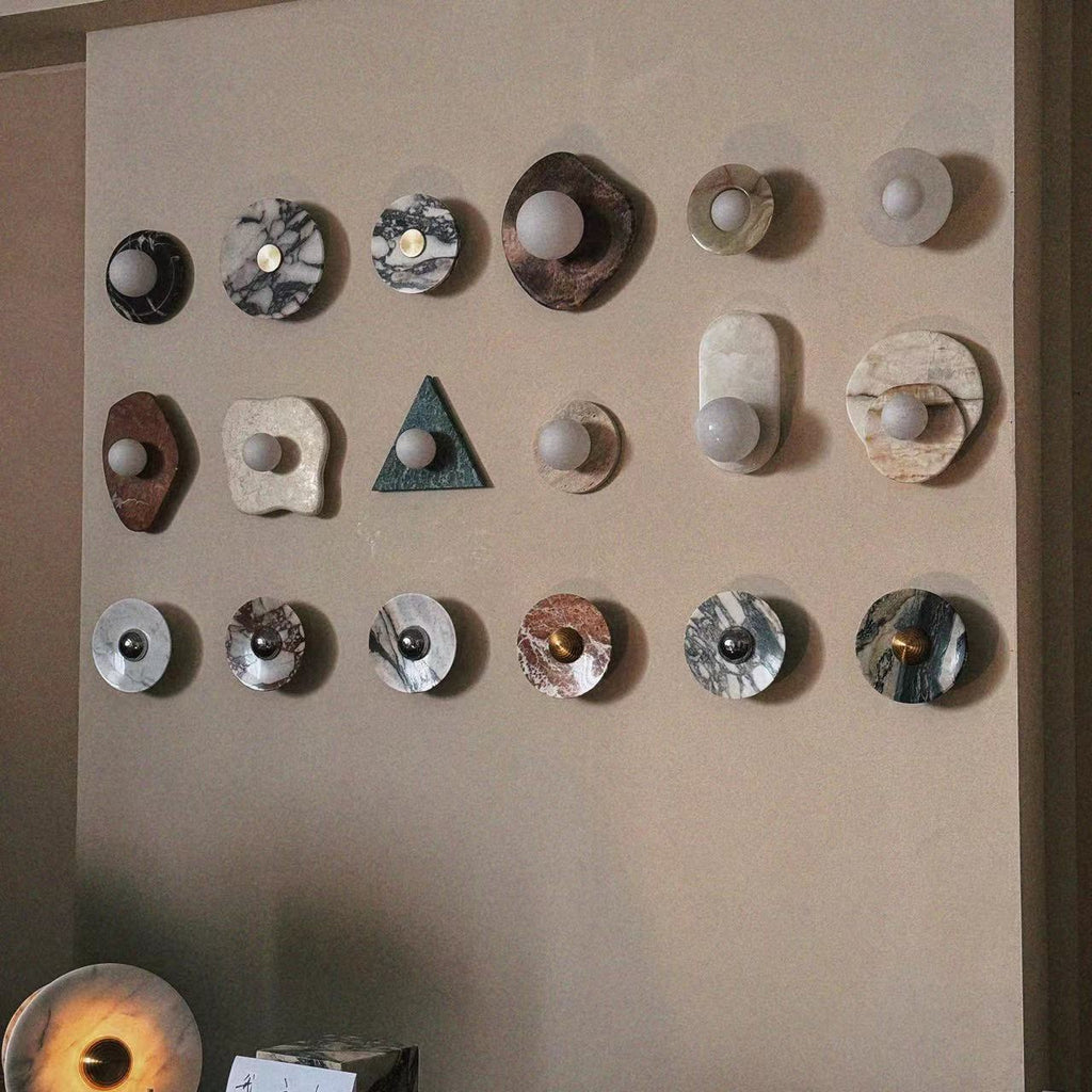 A beige display board of round stone, marble and wood finish samples echoes the marble disc style of the Clérachic wall light.