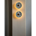 Two Clérachic marble wall lights glow warm amber, mounted vertically in a medium-close crop on a plain pillar wall.