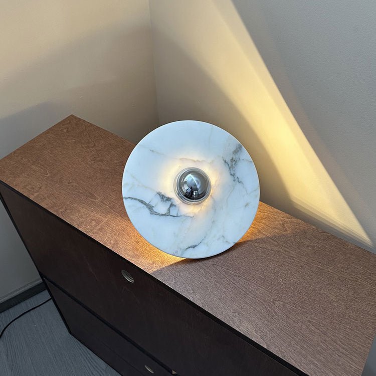 A paler, white-veined Clérachic marble disc with a chrome centre is propped on a wooden dresser, glowing warm underneath.
