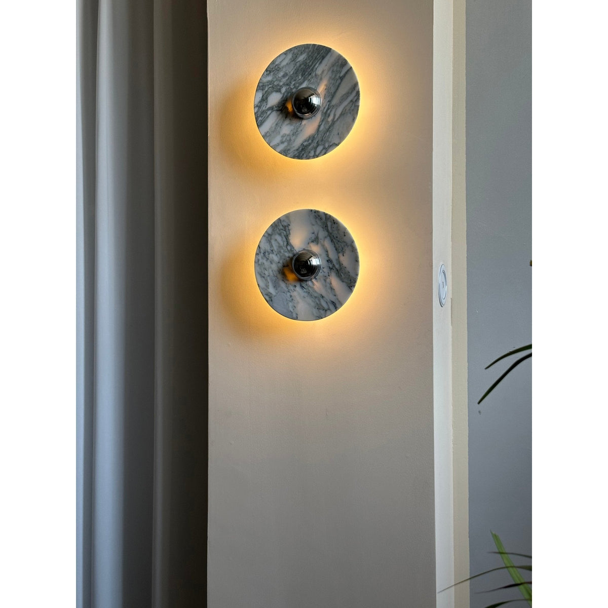 Two Clérachic marble wall lights glow warm amber on a wall pillar, with a light switch plate visible beside the lower fixture.