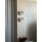 Two unlit, paler-veined Clérachic marble wall lights are seen from a distance beside a curtain and pillar edge.