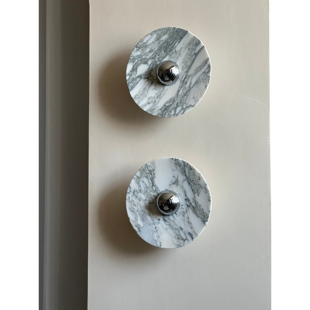 Close-up of two unlit Clérachic marble wall lights with grey veining, mounted vertically near a wall's edge.