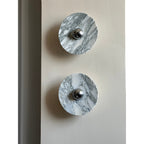 Close-up of two unlit Clérachic marble wall lights with grey veining, mounted vertically near a wall's edge.