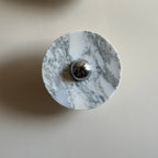 Daylight close-up of a single unlit Clérachic marble wall light, showing the grey veining and chrome centre knob in detail.