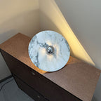 A Clérachic marble disc with a chrome centre is propped upright on a dresser corner, warm light glowing against the wall.