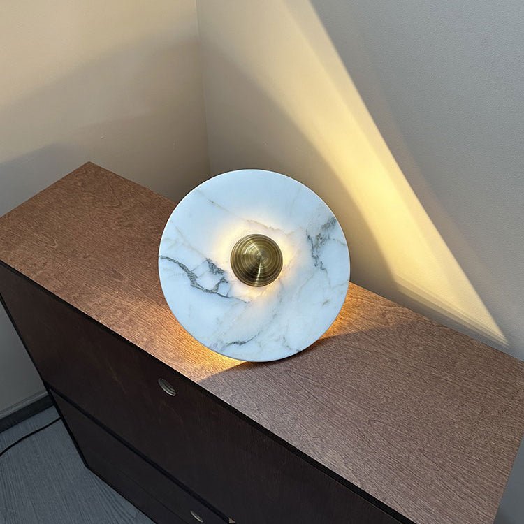 A white marble Clérachic disc with a brass centre knob rests propped on a dresser, warm light spilling into the room corner.