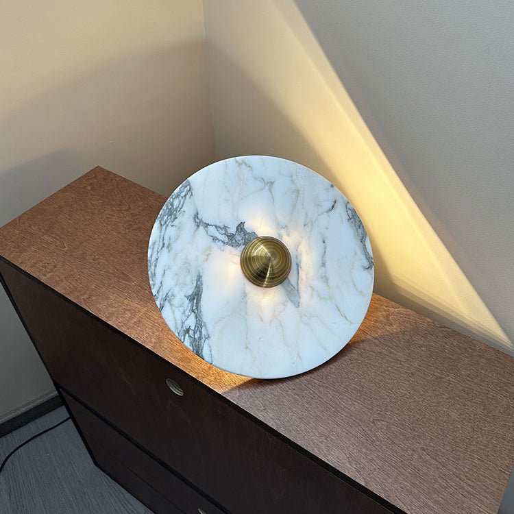 A wide view shows a Clérachic marble disc with a brass centre propped on a dresser corner, warm light raking up the wall behind it.