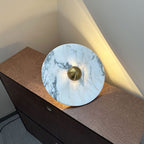 A wide view shows a Clérachic marble disc with a brass centre propped on a dresser corner, warm light raking up the wall behind it.