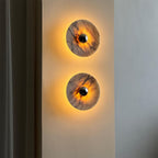 Two Clérachic marble disc wall lights stacked vertically in a narrow hallway nook, both glowing warm amber against the shadowed wall.