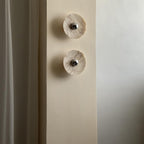 Two cream marble Clérachic wall lights, softly lit, are mounted vertically in a narrow wall nook beside a curtained window.