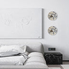 Two unlit Clérachic marble wall lights are mounted in a wide view beside a textured abstract canvas above a grey bed and dark cube nightstand.