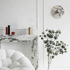 A tall, narrow crop frames the unlit Clérachic wall light above the fireplace mantel, with the candle holders and chair edge below.