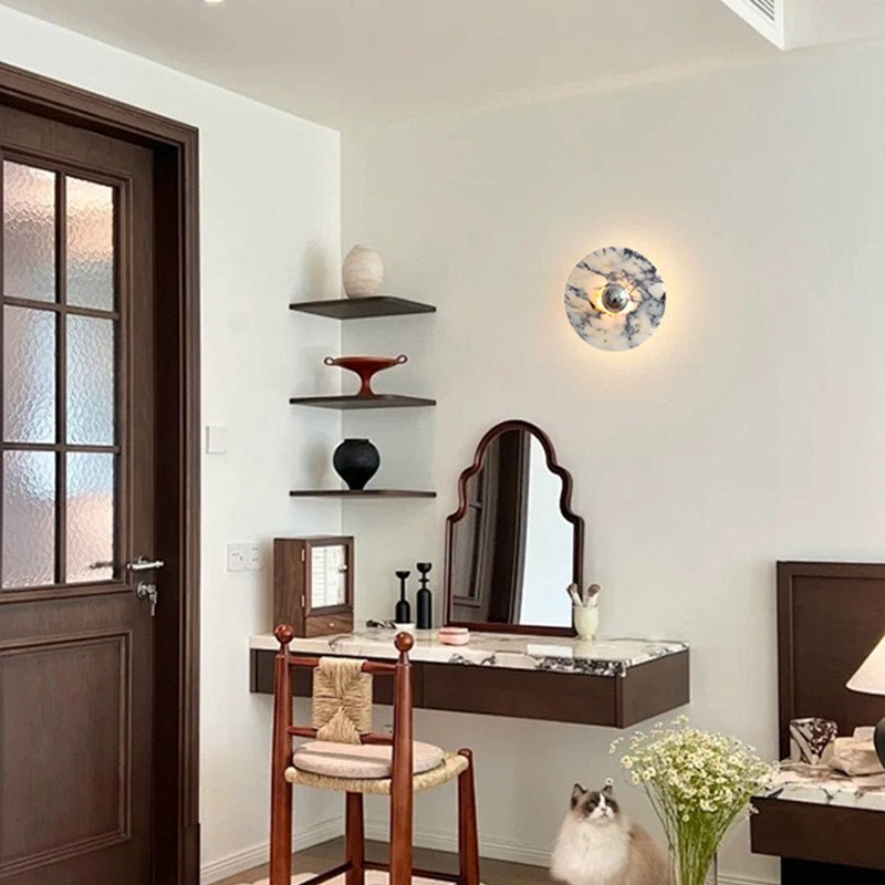 A taller crop of the same entryway shows the glowing Clérachic wall light, the rattan stool, mirror, cat and dressing table in full.