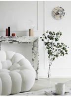 The widest crop of this fireplace corner shows the unlit Clérachic wall light, the bouclé chair, a teacup on the floor and a potted branch.