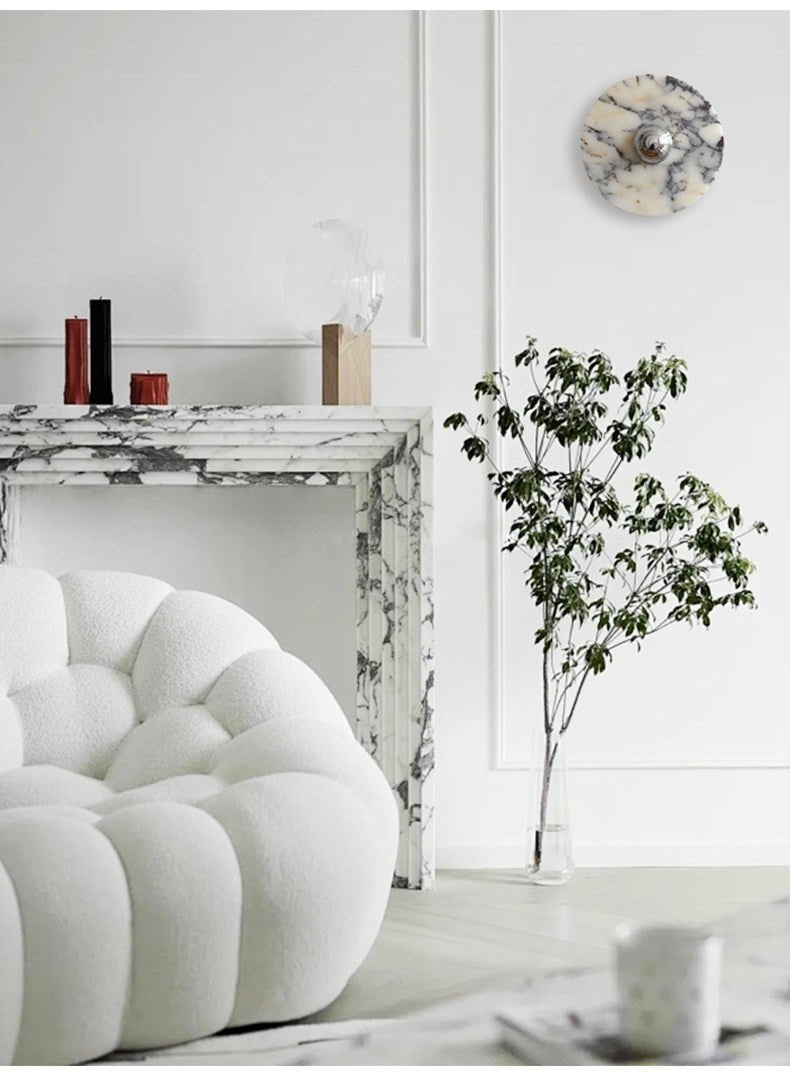 The widest crop of this fireplace corner shows the unlit Clérachic wall light, the bouclé chair, a teacup on the floor and a potted branch.