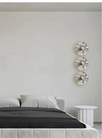 Three Clérachic marble wall lights are stacked vertically in a bedroom corner, all glowing warm amber beside a round side table.