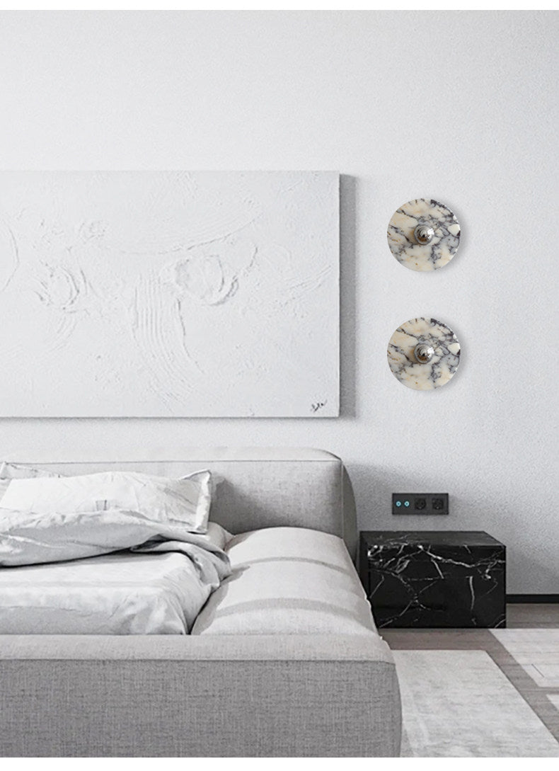 A tighter crop of the same bedroom nook shows the two unlit Clérachic wall lights beside the abstract canvas and marble nightstand cube.
