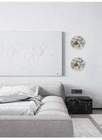 A tighter crop of the same bedroom nook shows the two unlit Clérachic wall lights beside the abstract canvas and marble nightstand cube.