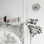 A wider view shows the same unlit Clérachic wall light above the fireplace, with two candle holders, a potted branch and the full bouclé chair.