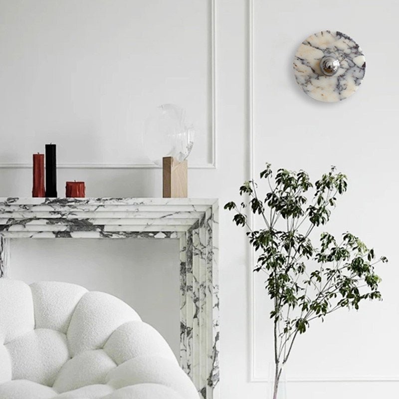 A wider view shows the same unlit Clérachic wall light above the fireplace, with two candle holders, a potted branch and the full bouclé chair.