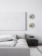 The same two Clérachic wall lights now glow warm amber beside the abstract canvas, above the grey bed and dark marble nightstand cube.