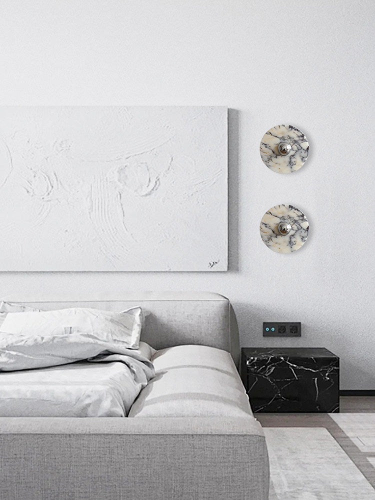 The same two Clérachic wall lights now glow warm amber beside the abstract canvas, above the grey bed and dark marble nightstand cube.